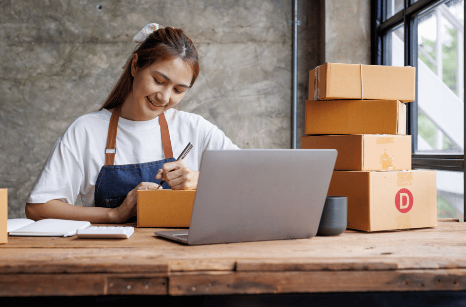 Imagen que representa a un emprendedor trabajando desde su hogar, rodeado de elementos relacionados con la logística de su pequeño negocio. Se ve a un comerciante organizando su inventario mientras su hija observa con curiosidad. La imagen refleja el espíritu emprendedor, la gestión de servicios y la dinámica empresarial que se desarrolla en un ambiente familiar